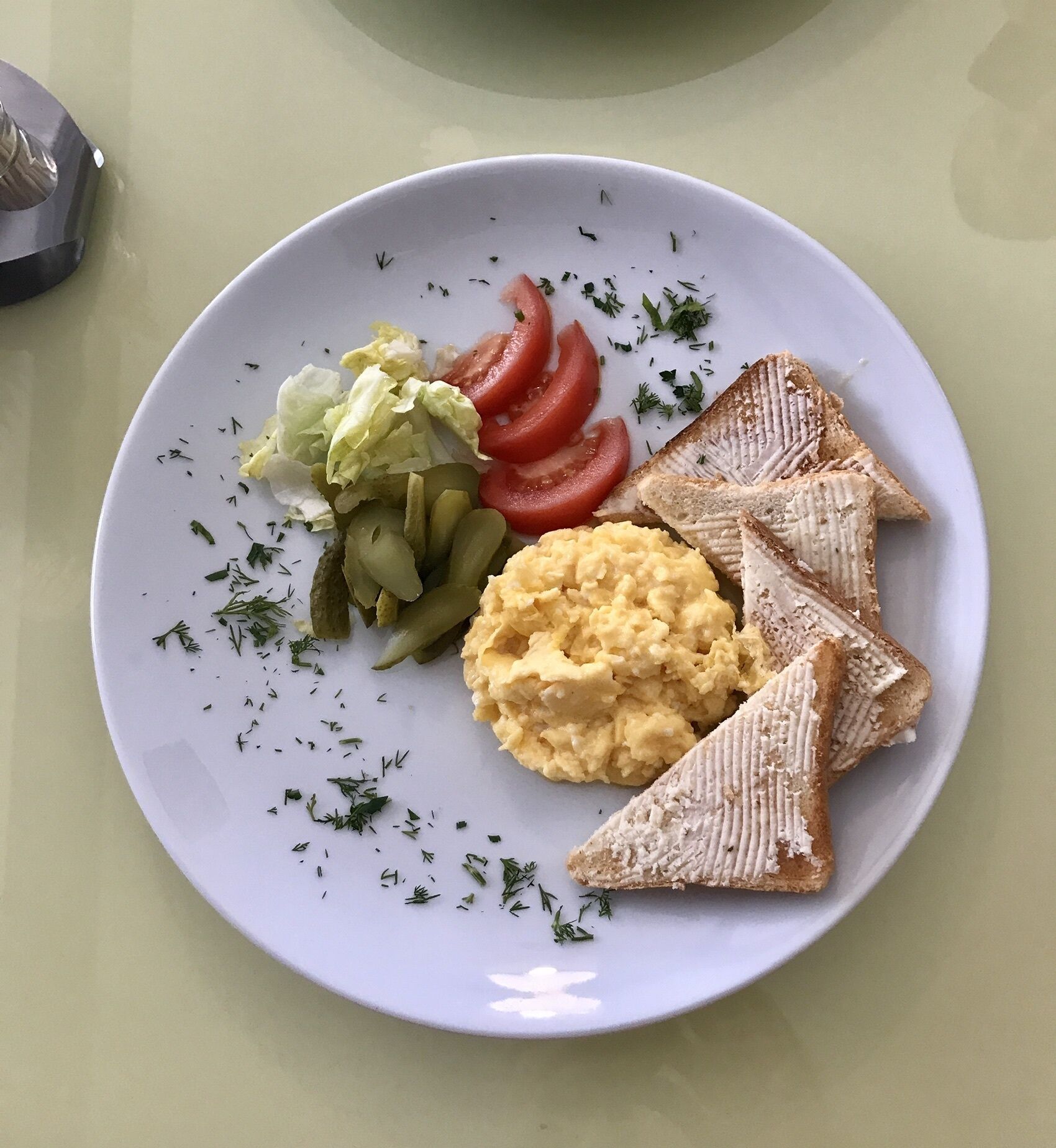 A plate with scrambled eggs, pickles, lettuce, tomato slices, and toast.