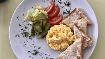 A plate with scrambled eggs, pickles, lettuce, tomato slices, and toast.