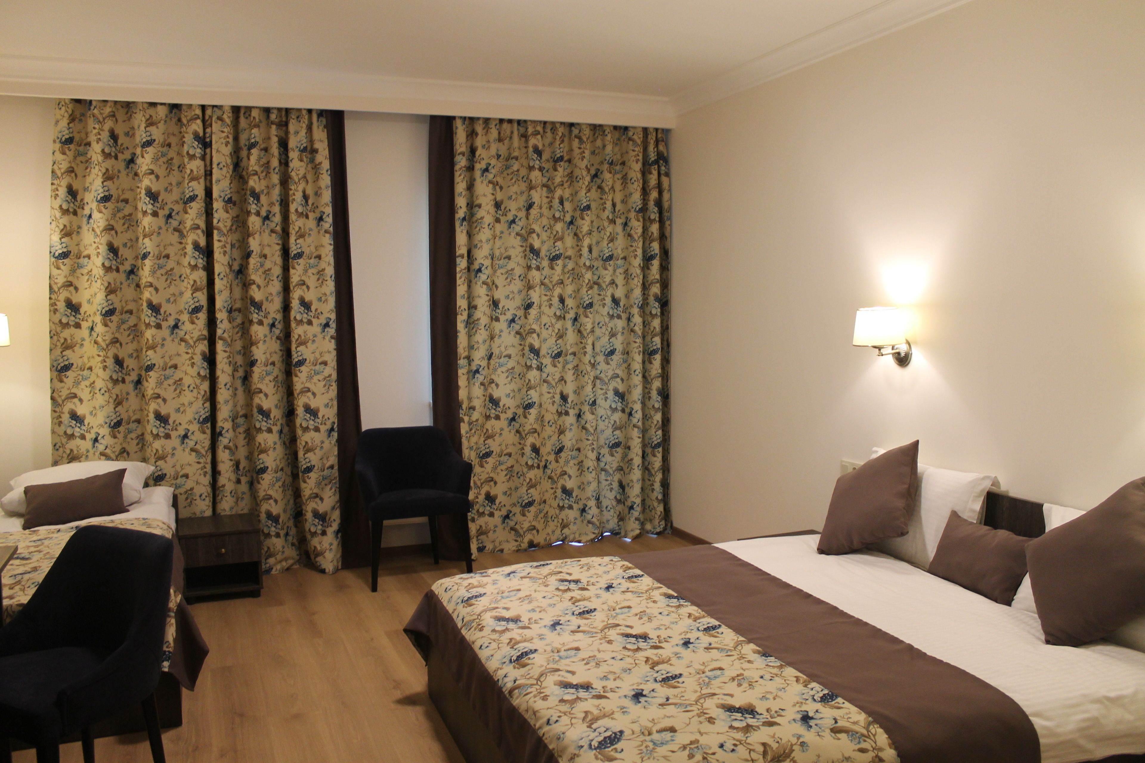 A hotel room with a bed, a chair, a nightstand, and curtains.