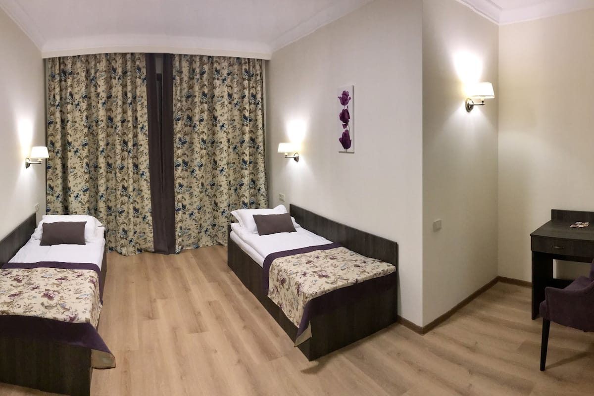 Ein Zimmer mit zwei Einzelbetten, einem Schreibtisch, einem Stuhl und einem Vorhang mit Blumenmuster.