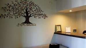 A reception area with a wall-mounted tree decal, a counter with framed pictures, and a white sofa. - Non-Stop Hotel (Boryspil)