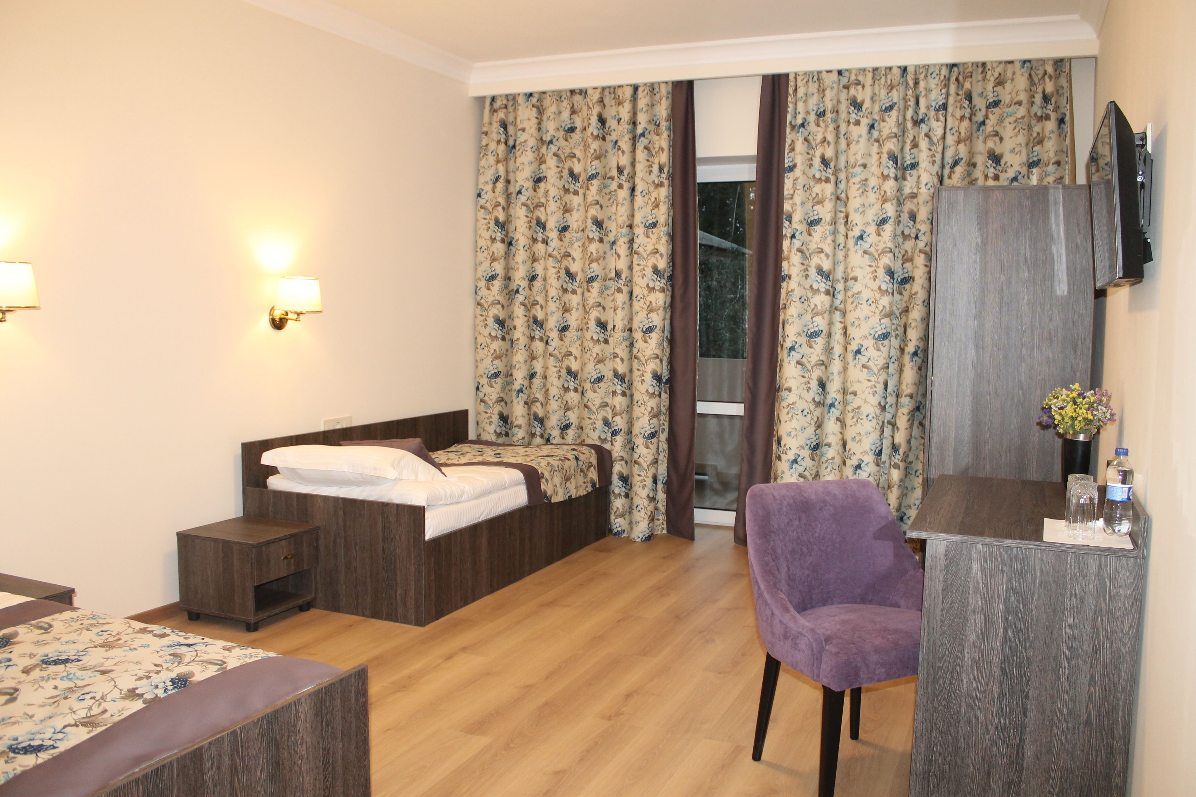 A hotel room with a bed, a desk with a chair, a TV, and a window with curtains.