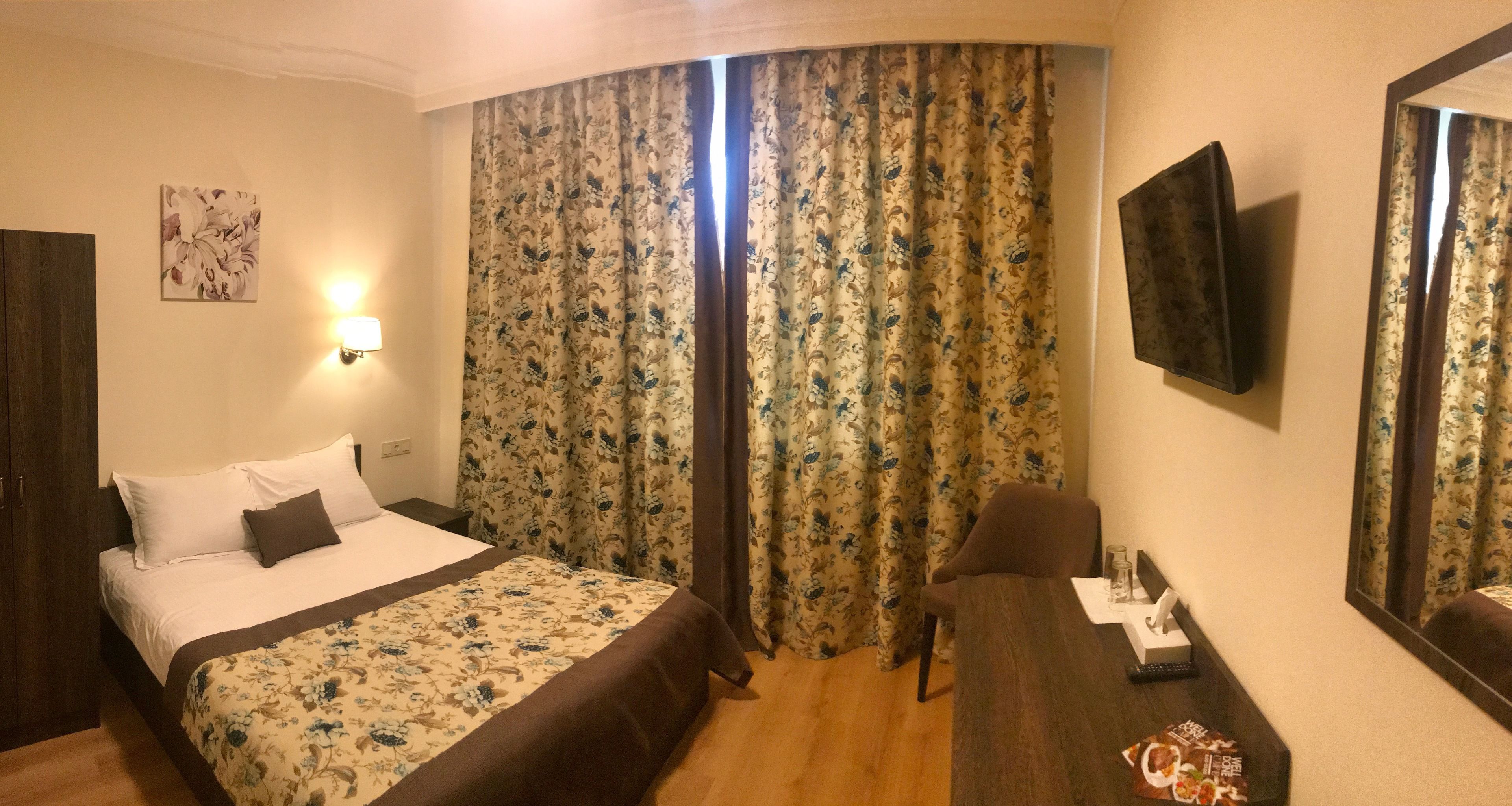 A hotel room with a bed, a desk, a chair, a TV, and curtains.
