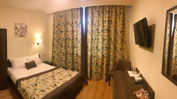 A hotel room with a bed, a desk, a chair, a TV, and curtains.