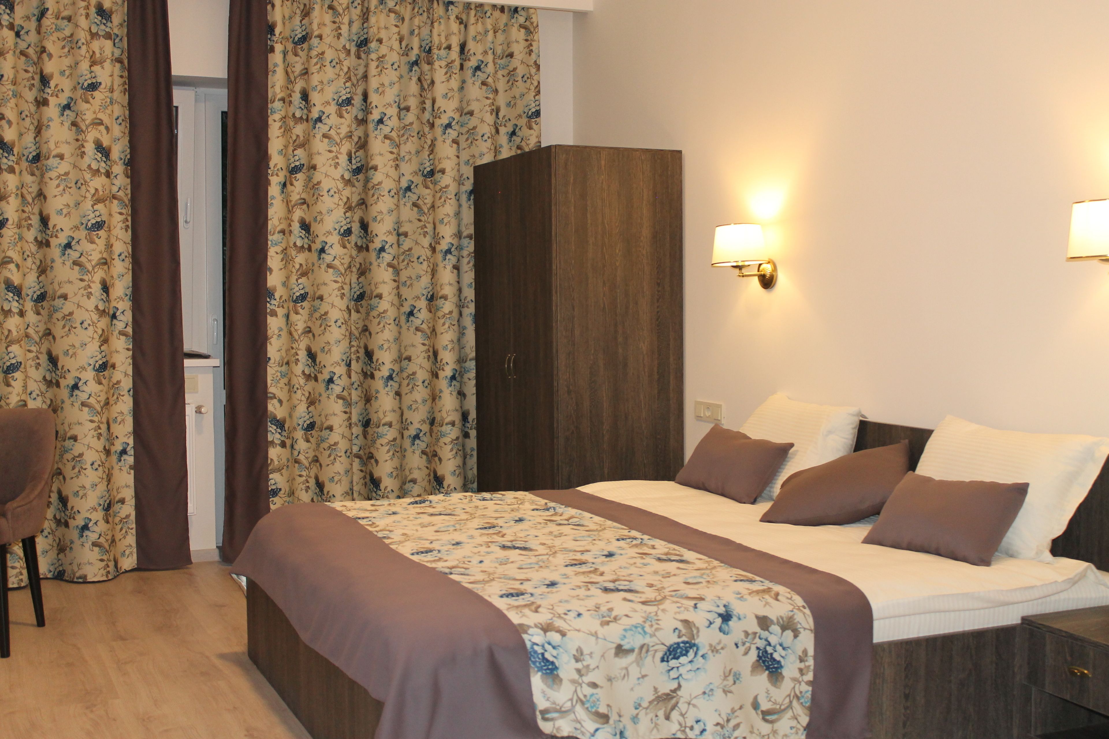 A hotel room with a bed, a wardrobe, a chair, and curtains.