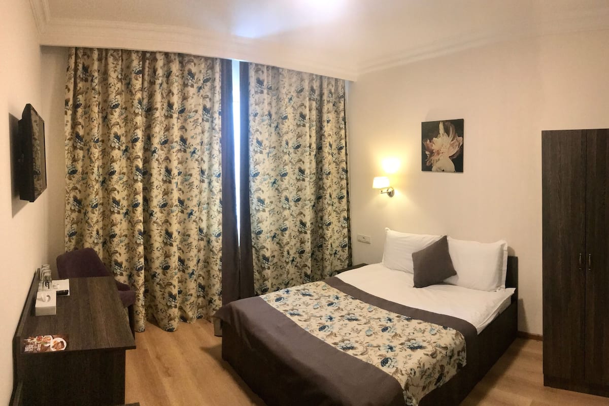 Ein Hotelzimmer mit Bett, Schreibtisch mit Lampe, einem Bild an der Wand und einem Kleiderschrank.