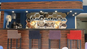 A bar area with a wooden counter, hexagonal mirrors, and bar stools in various colors. - Non-Stop Hotel (Boryspil)