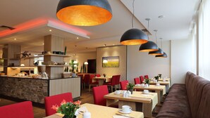 Un restaurante moderno con mesas altas, sillas rojas y una isla central con electrodomésticos de cocina.
