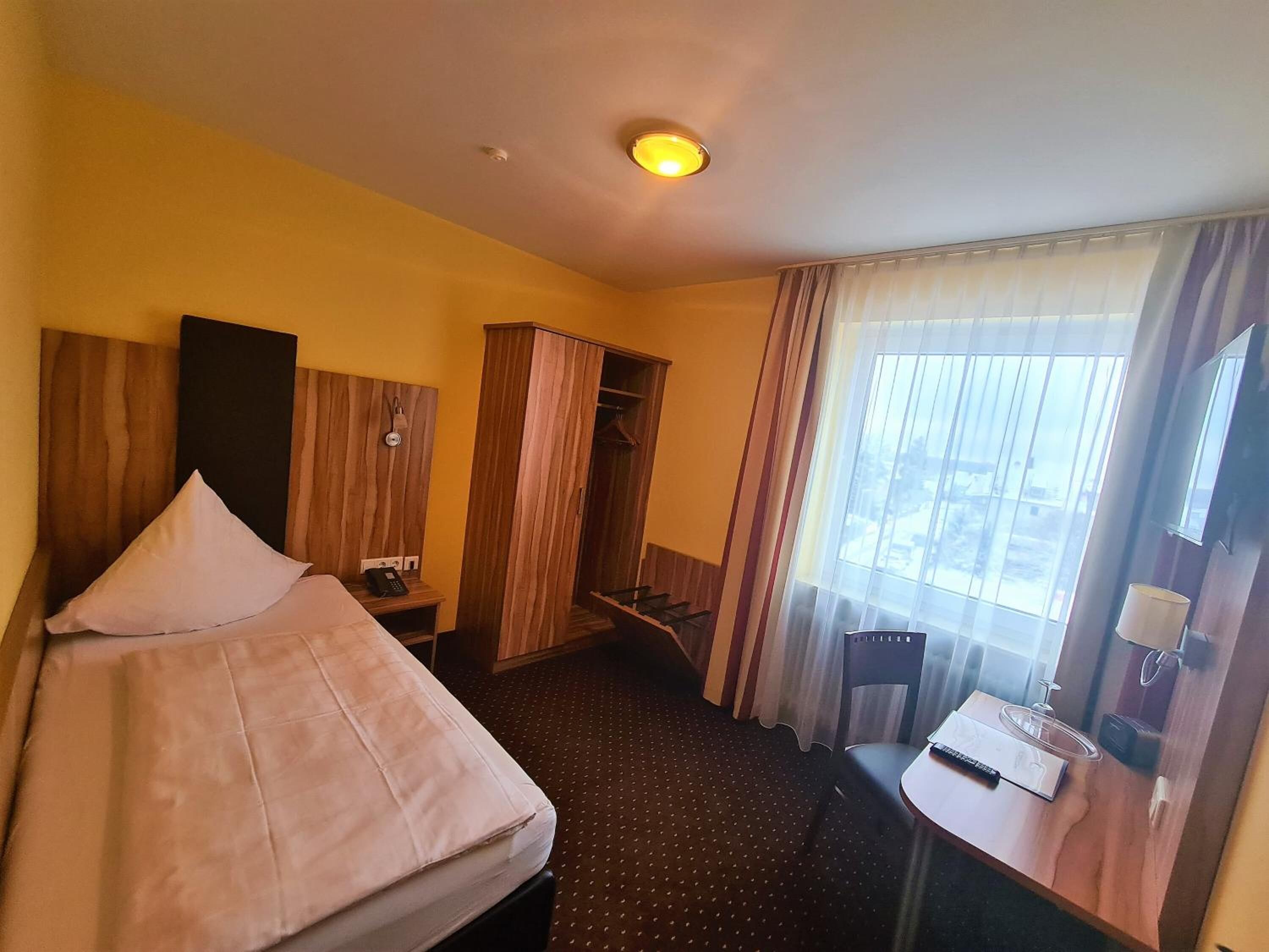 A hotel room with a bed, a desk, a wardrobe, and a window with curtains.