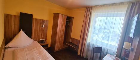 A hotel room with a bed, a desk, a wardrobe, and a window with curtains.