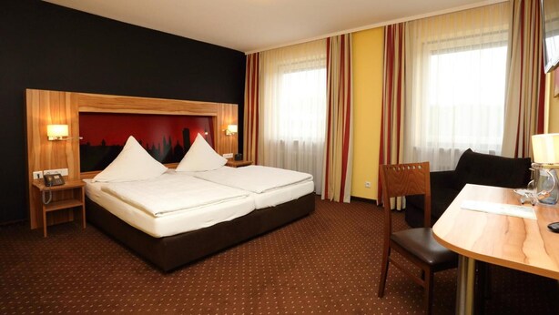 Habitación de hotel con una cama grande, un escritorio con silla, una mesita de noche y un televisor instalado en la pared.