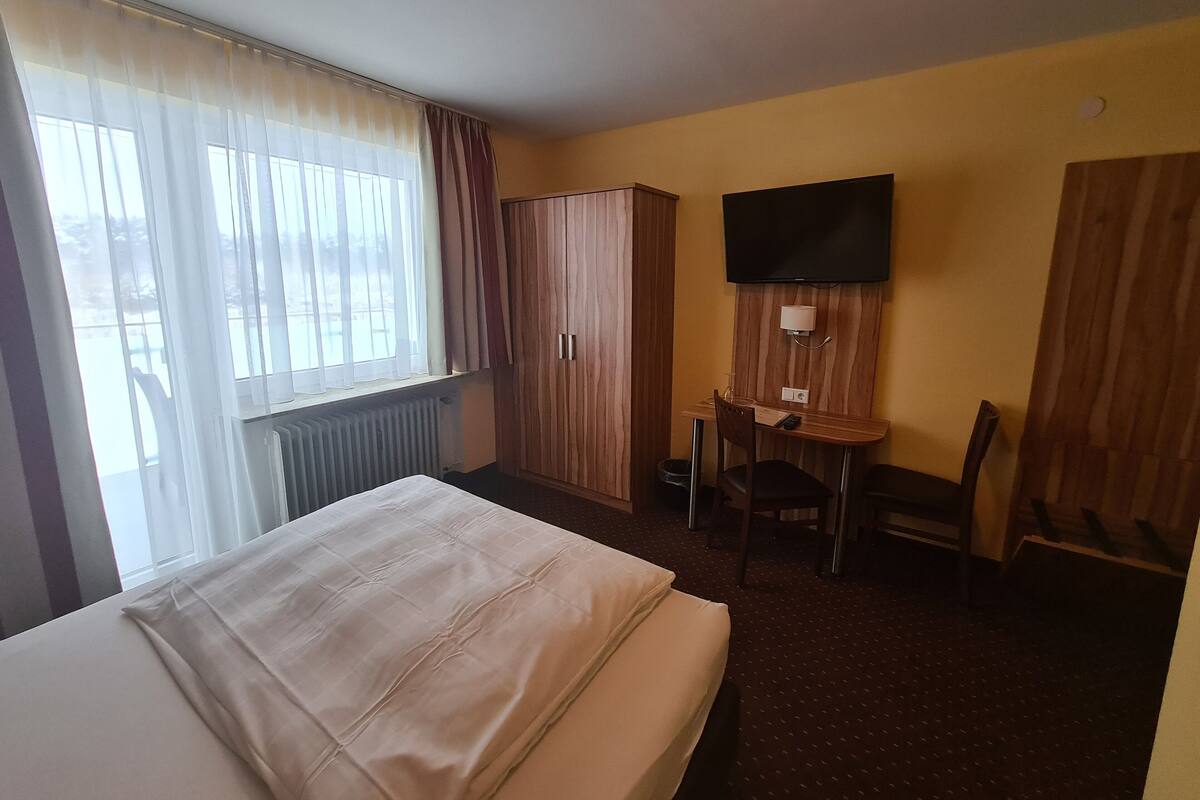Ein Hotelzimmer mit einem Bett, einem Schreibtisch mit Stuhl, einem an der Wand befestigten Fernseher und einem Kleiderschrank.