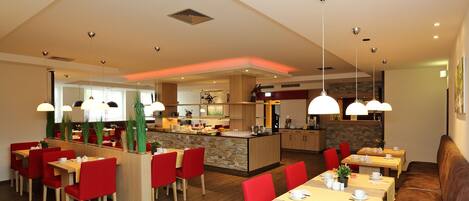 A modern dining area with red chairs, wooden tables, and pendant lighting.