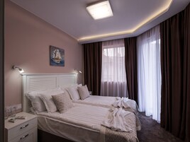 Habitación de hotel con cama, mesitas de noche, un cuadro y una ventana con cortinas.