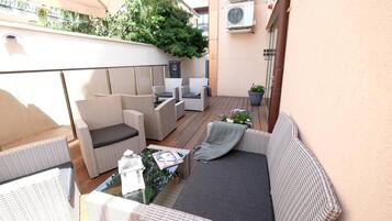 A covered outdoor seating area with wicker furniture, a glass table, and potted plants.