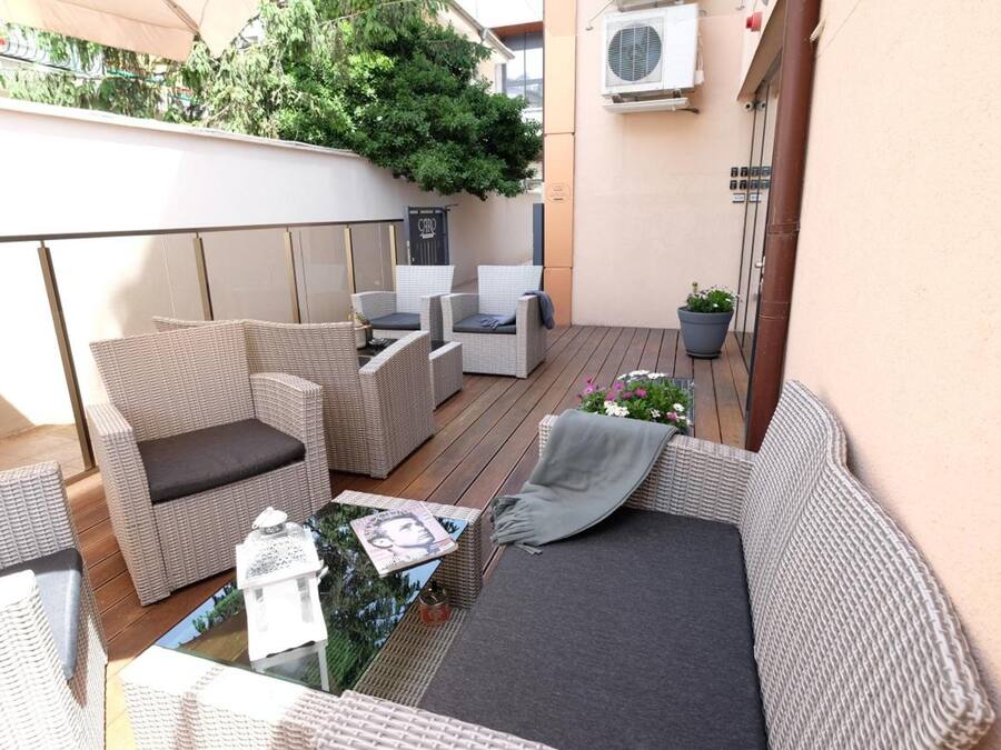 A covered outdoor seating area with wicker furniture, a glass table, and potted plants.
