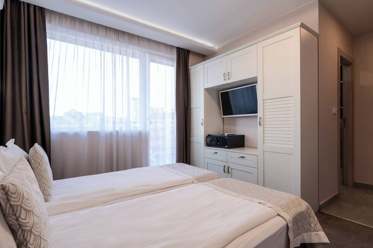 A hotel room with two beds, a TV on a cabinet, and a view of the city through large windows.