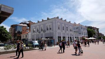 A hotel with a modern glass facade, a traditional white building with multiple stories, and a paved pedestrian area with people walking.