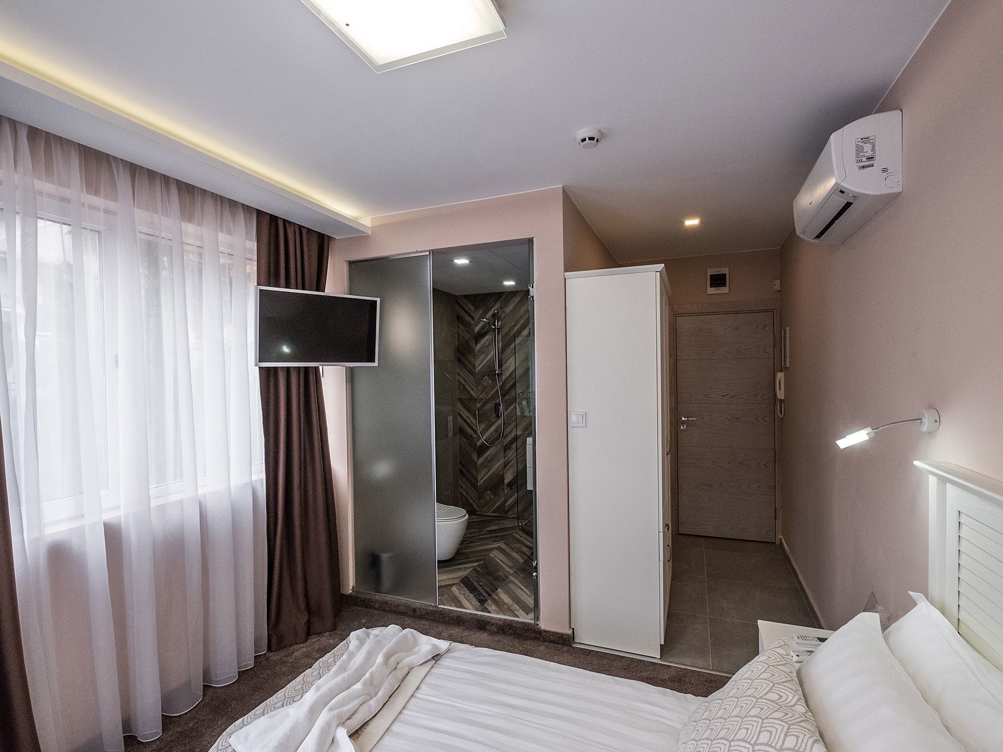 Ein Hotelzimmer mit Bett, Fernseher, Kleiderschrank, Duschbereich und Klimaanlage.