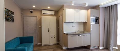 A modern kitchen with white cabinets, a microwave, and a sink. There is a blue sofa and a small white table in the living area.