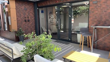 Un espace patio avec des sièges d’extérieur, une entrée avec une porte vitrée et un mur en briques.