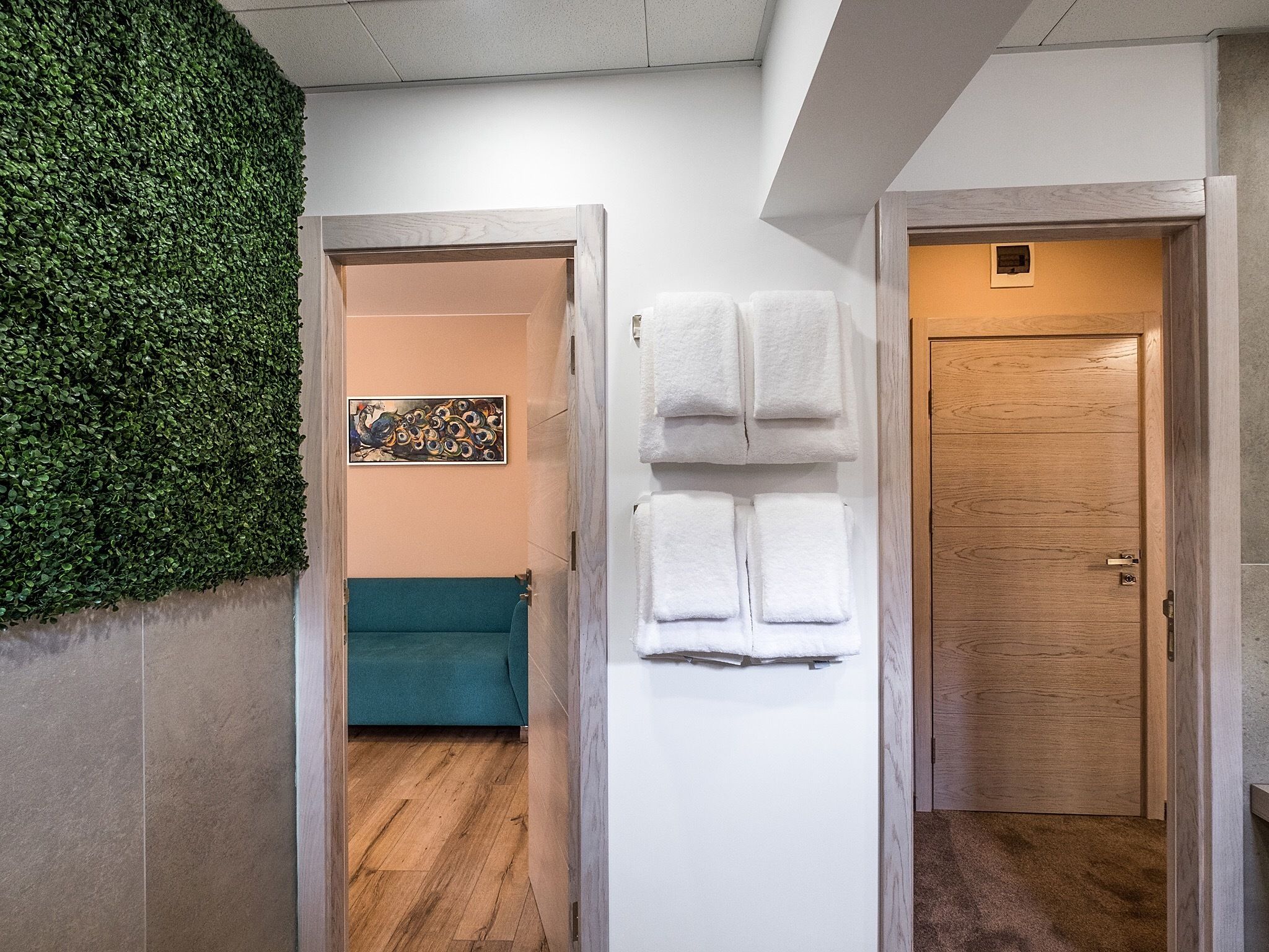 A hallway with a green wall, a teal sofa, a white door, and a wooden door.