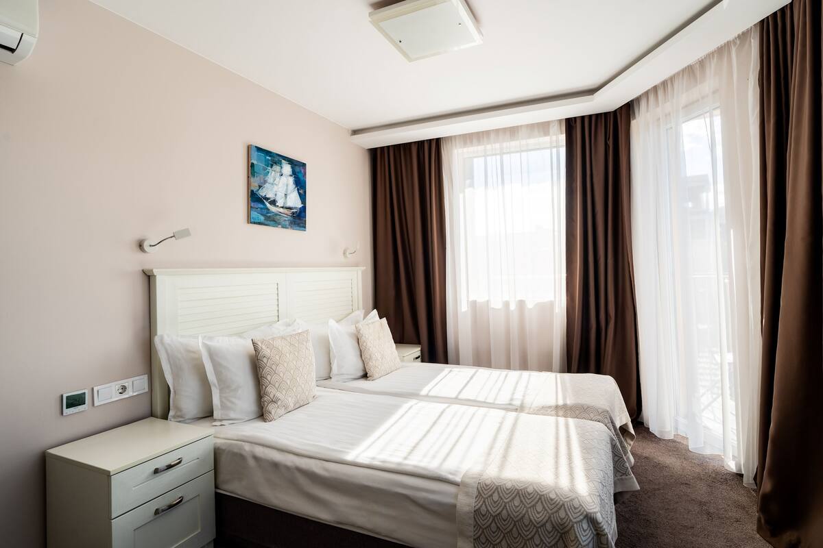 A hotel room with a large bed, a bedside table, a nightstand, and a painting on the wall.