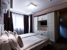 Una habitación de hotel con dos camas, un armario, un televisor y una ventana con cortinas.