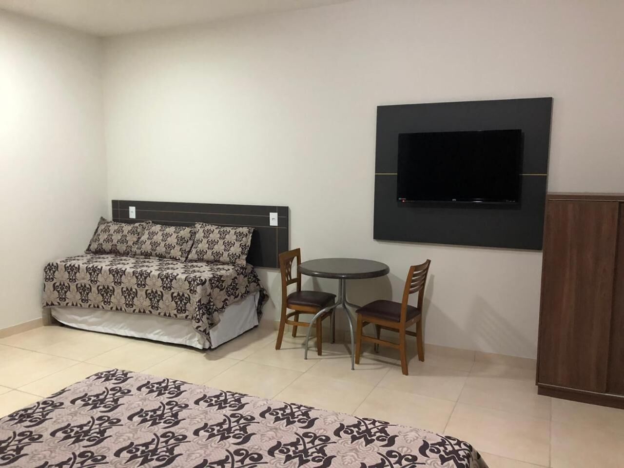 Ein Schlafzimmer mit einem Bett, einem runden Tisch mit zwei Stühlen, einem an der Wand montierten Fernseher und einem Kleiderschrank.