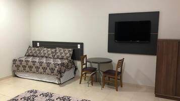 Ein Schlafzimmer mit einem Bett, einem runden Tisch mit zwei Stühlen, einem an der Wand montierten Fernseher und einem Kleiderschrank.