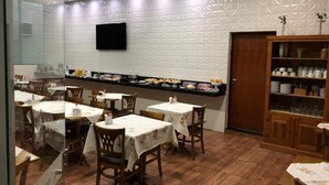 Un restaurant avec des tables et des chaises rondes, un buffet et un téléviseur fixé au mur.