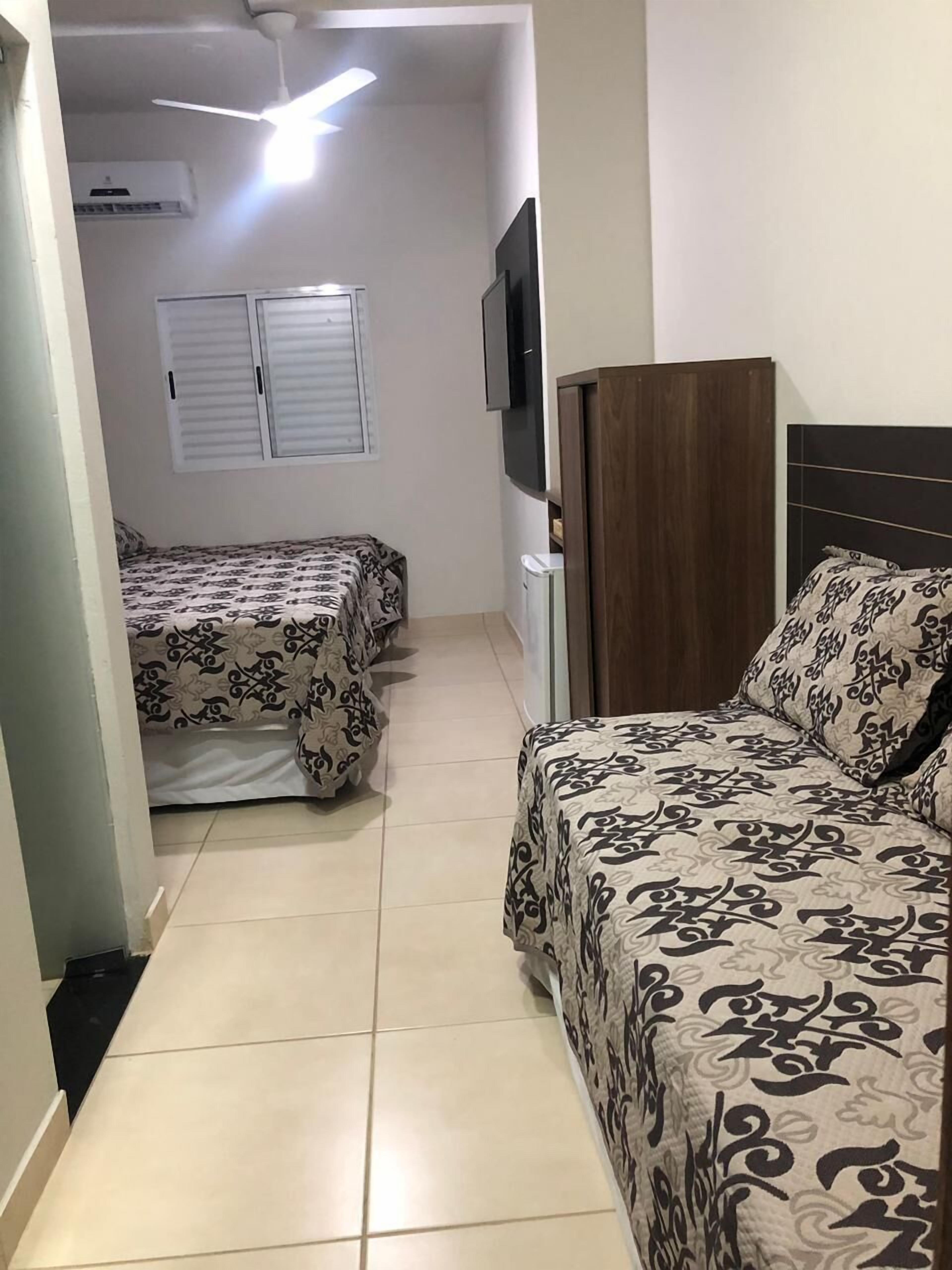 A hotel room with two beds, a TV, a ceiling fan, and an air conditioning unit.