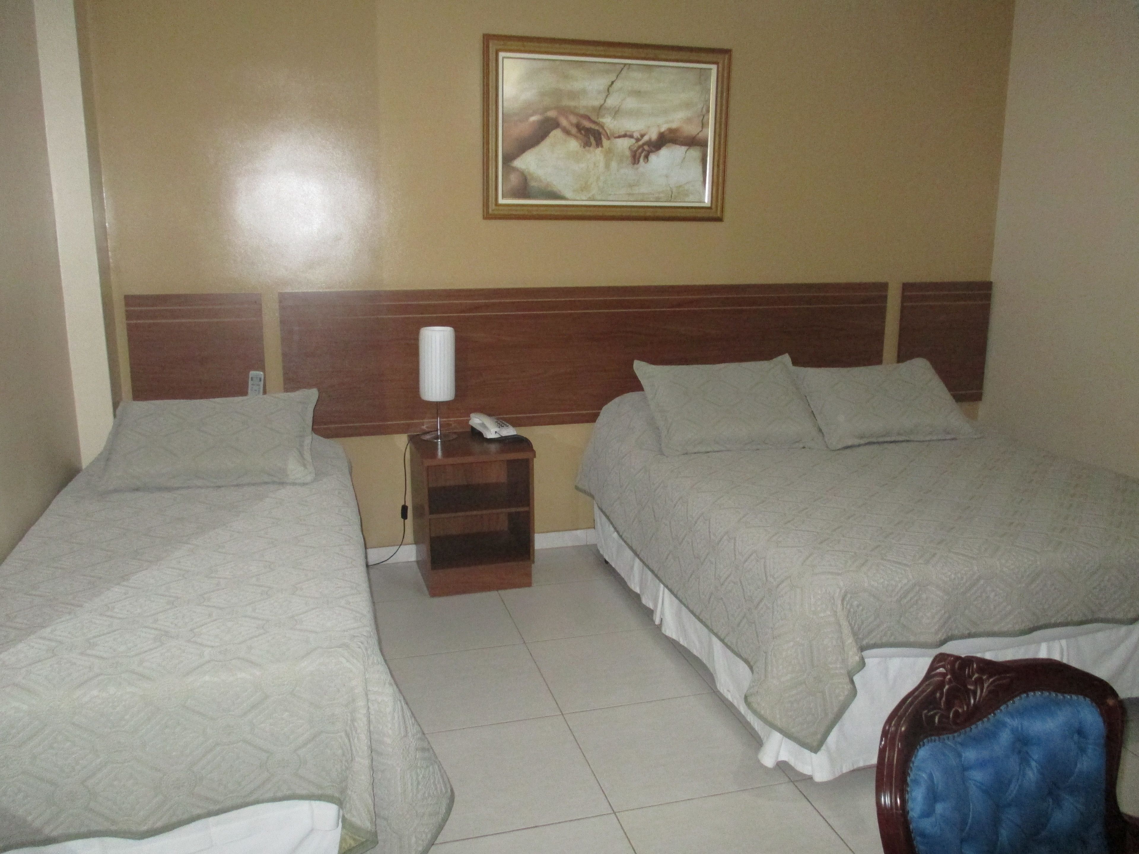 A hotel room with two beds, a nightstand with a lamp and phone, and a painting on the wall.