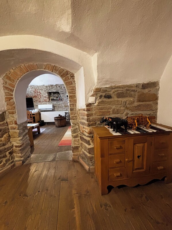A room with a stone archway leading to another space, wooden flooring, and a wooden cabinet with drawers. - Taschler Haus Boutique (Sighisoara)