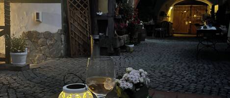 An outdoor seating area with a table, a glass of white wine, a decorative lantern, and a potted plant.