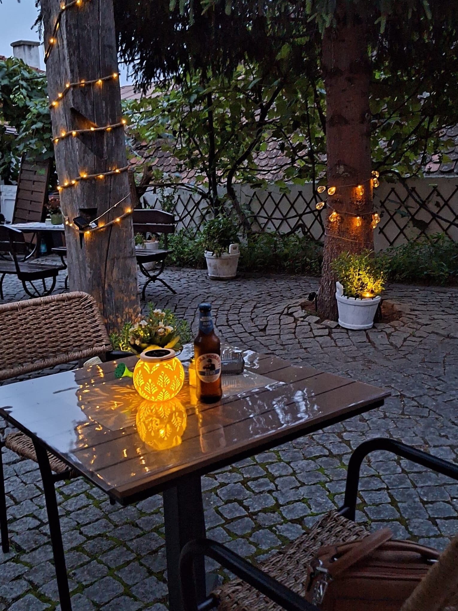 An outdoor patio area with a table, chairs, string lights, and potted plants.