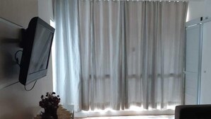A modern living room with a flat-screen TV mounted on the wall, a sofa, and a large window with sheer curtains. - Canto do Pescador (Bombinhas)