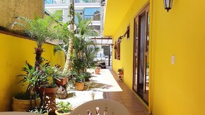 A narrow outdoor corridor with yellow walls, potted plants, and a white chair. - Canto do Pescador (Bombinhas)