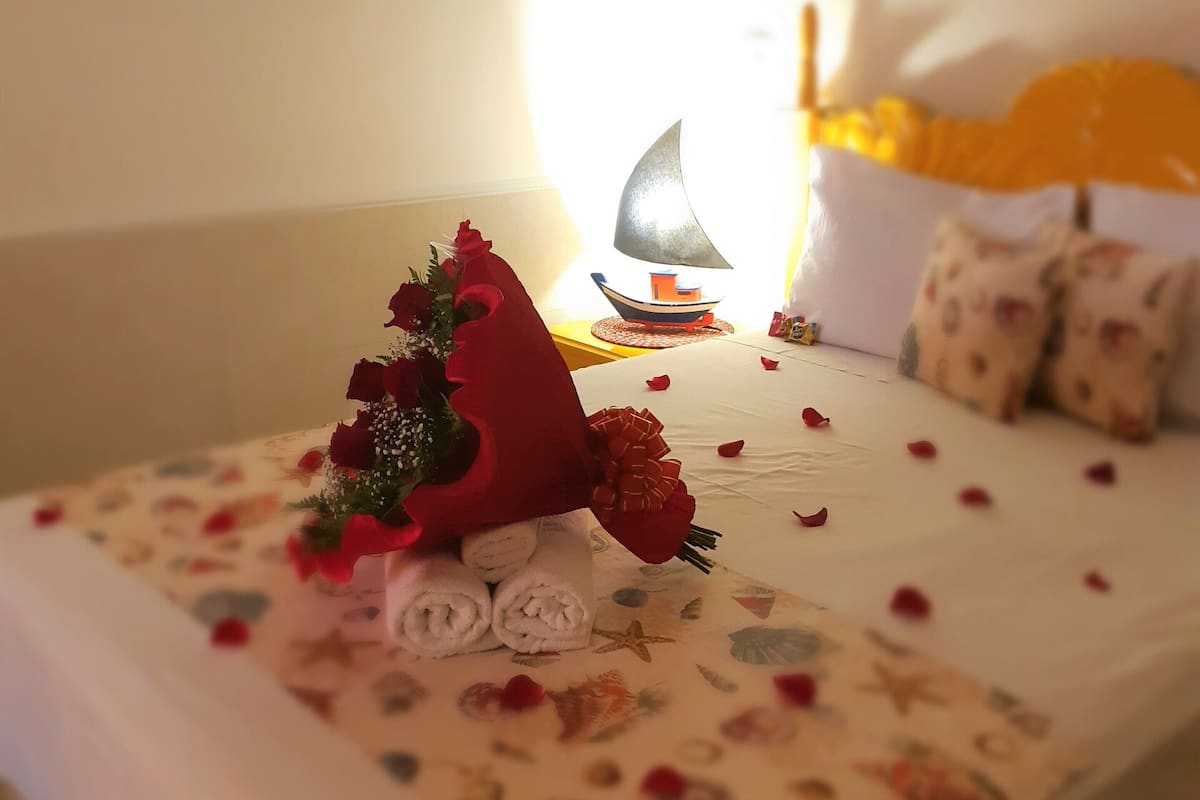 A neatly made bed with a floral bedspread, a bouquet of red roses, and a small sailboat decoration.