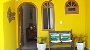 A bright yellow building with a wooden bench and two potted plants. - Canto do Pescador (Bombinhas)