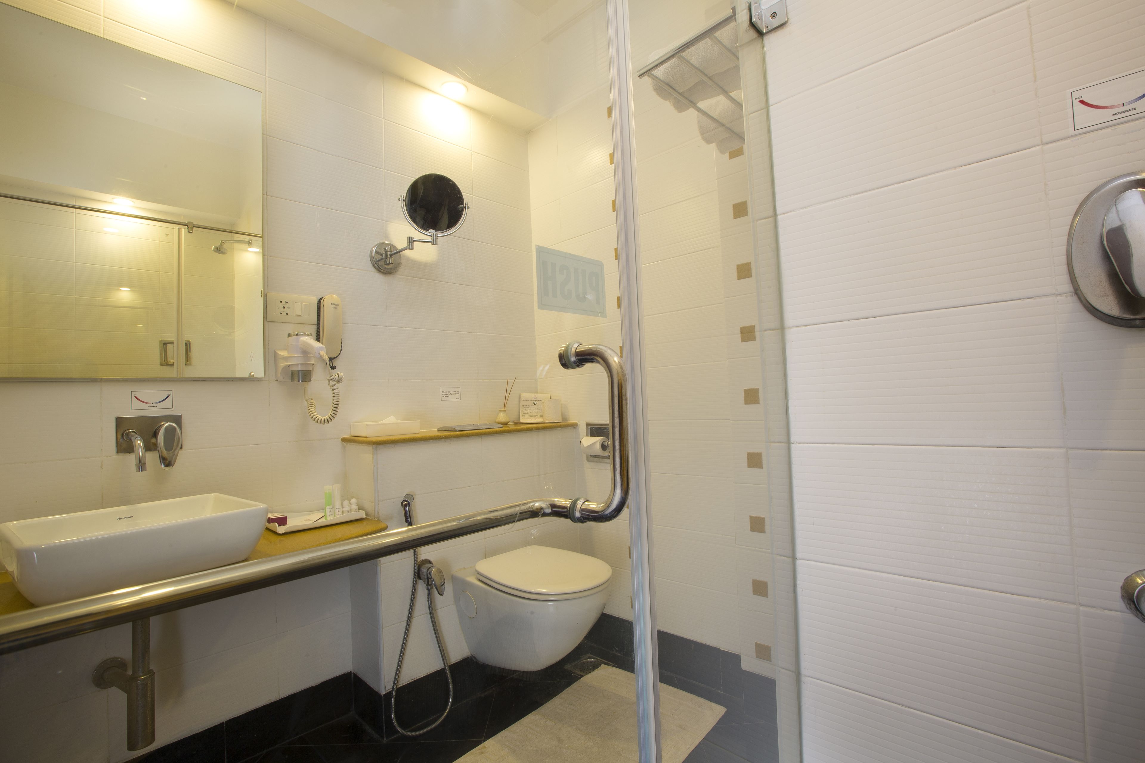 Ein Badezimmer mit weißem Waschbecken, Toilette, Spiegel und Duschbereich.