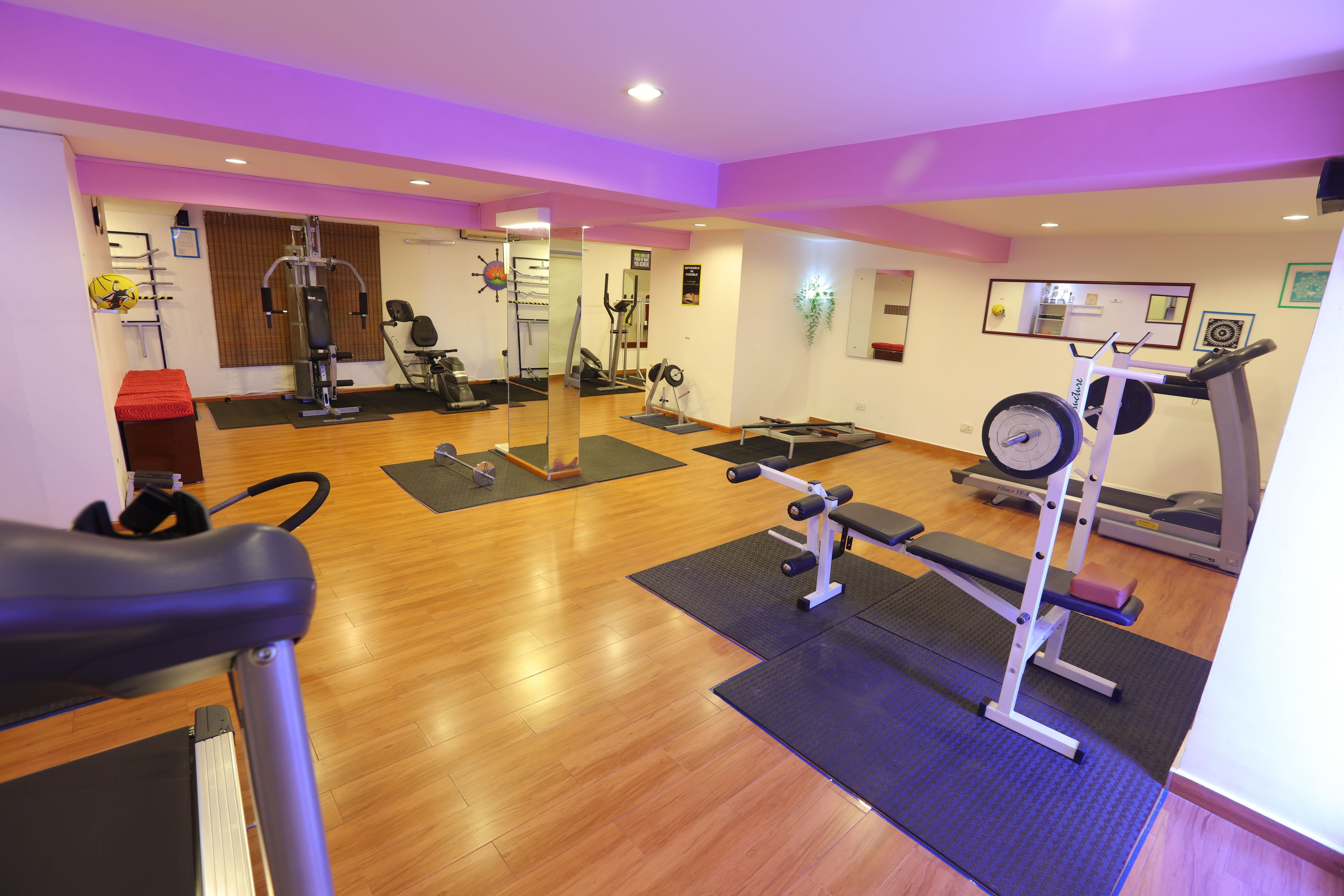 Uma academia com equipamentos de exercício, piso de madeira e iluminação roxa.