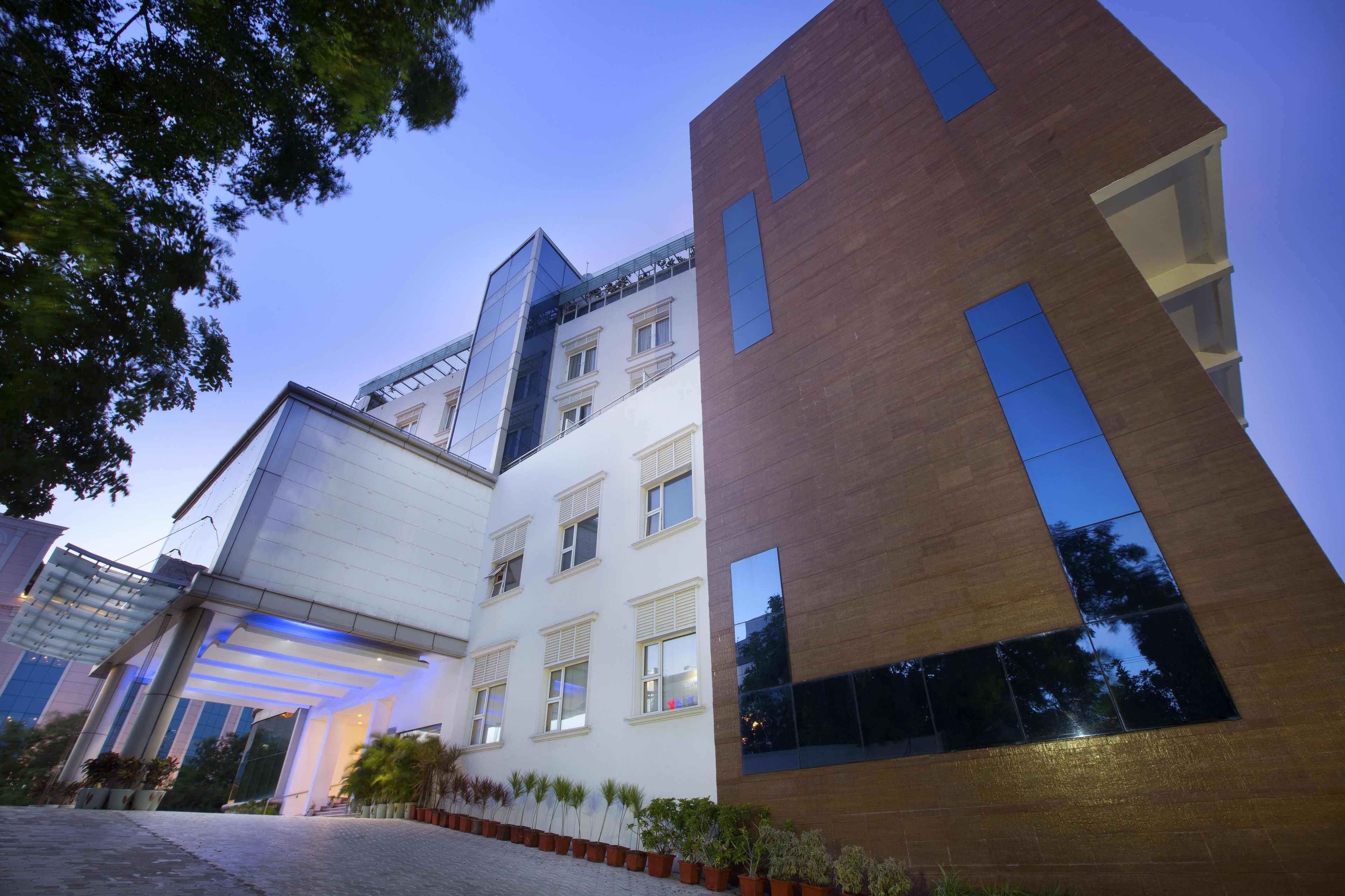 Un edificio moderno con fachadas de vidrio y ladrillo, ventanas amplias y un área exterior bien cuidada con plantas en macetas.