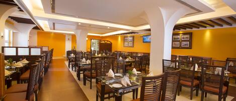 Un restaurant spacieux, doté de nombreuses tables et chaises, de hauts plafonds avec des luminaires encastrés et d’une décoration aux couleurs chaudes.