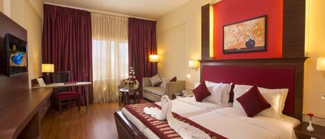 A hotel room with a large bed, a desk, a chair, and a TV.