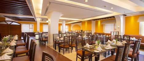 A spacious dining area with multiple tables and chairs, high ceilings with recessed lighting, and a modern architectural design.