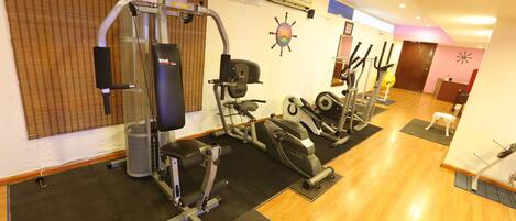 A gym with various exercise machines, a wall-mounted air conditioner, and a wooden floor.
