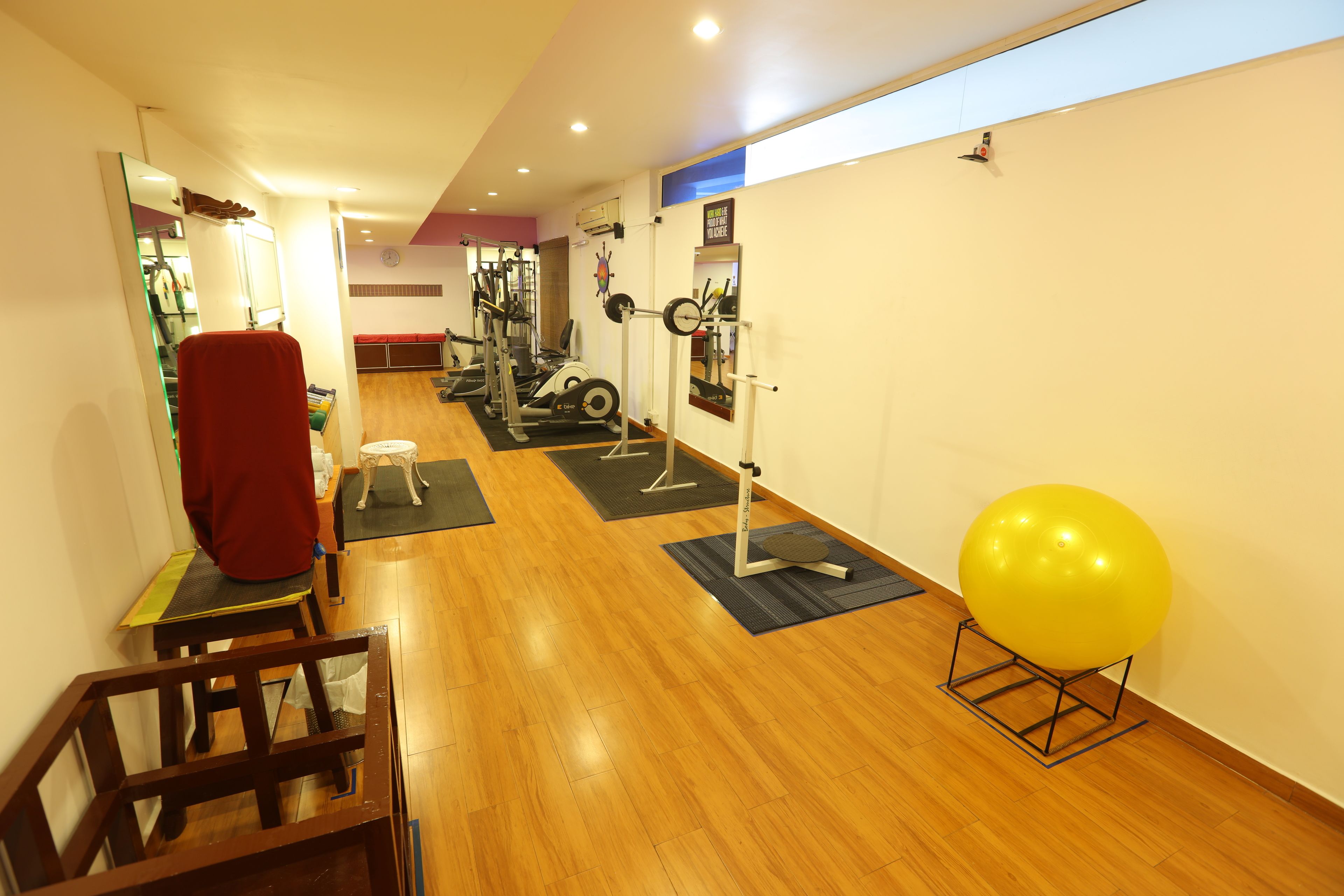 Un gimnasio con suelo de madera, equipo de ejercicio y una pelota de entrenamiento amarilla.