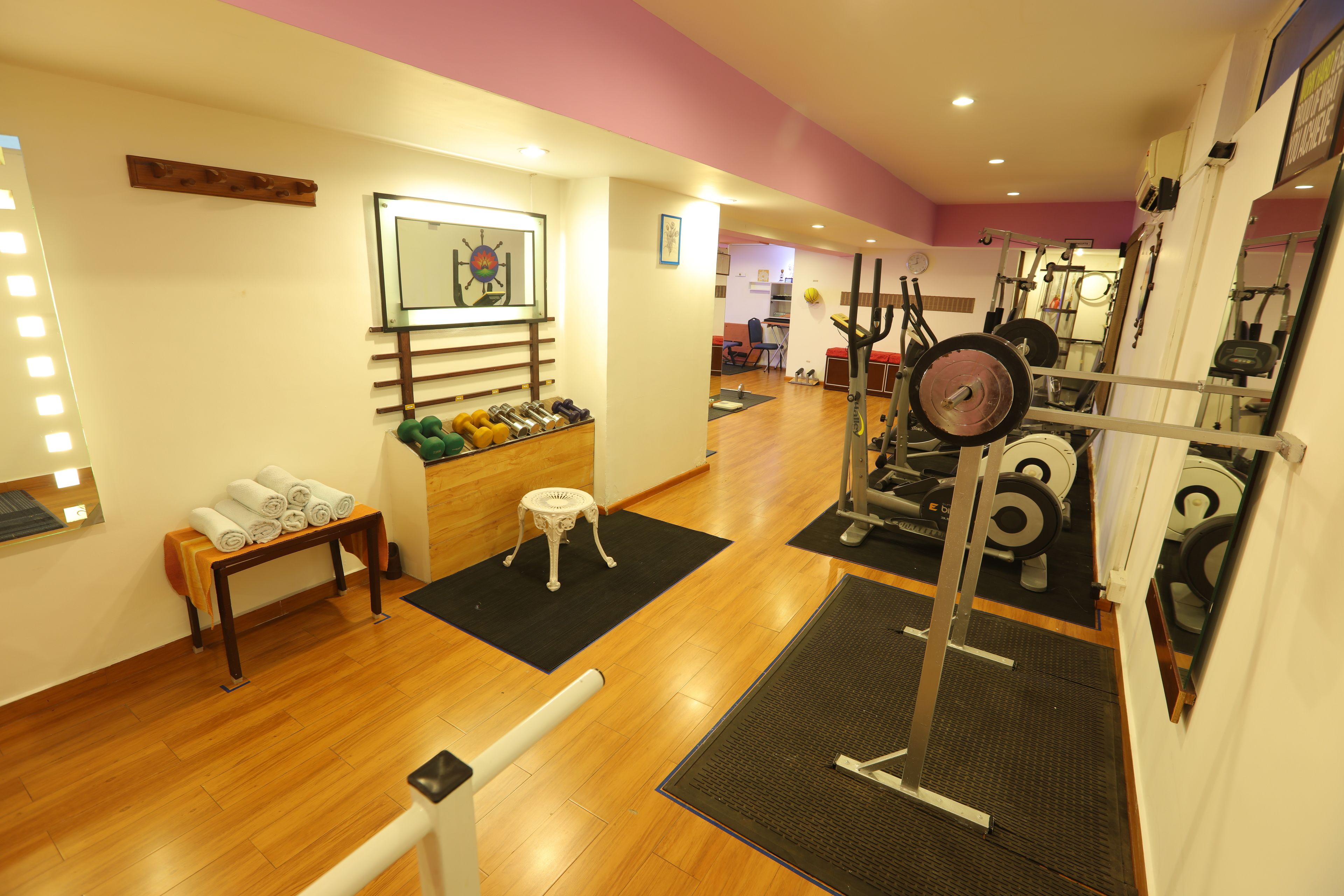 Ein Fitnessraum mit Trainingsgeräten, einer Bank mit Handtüchern und einem Spiegel an der Wand.