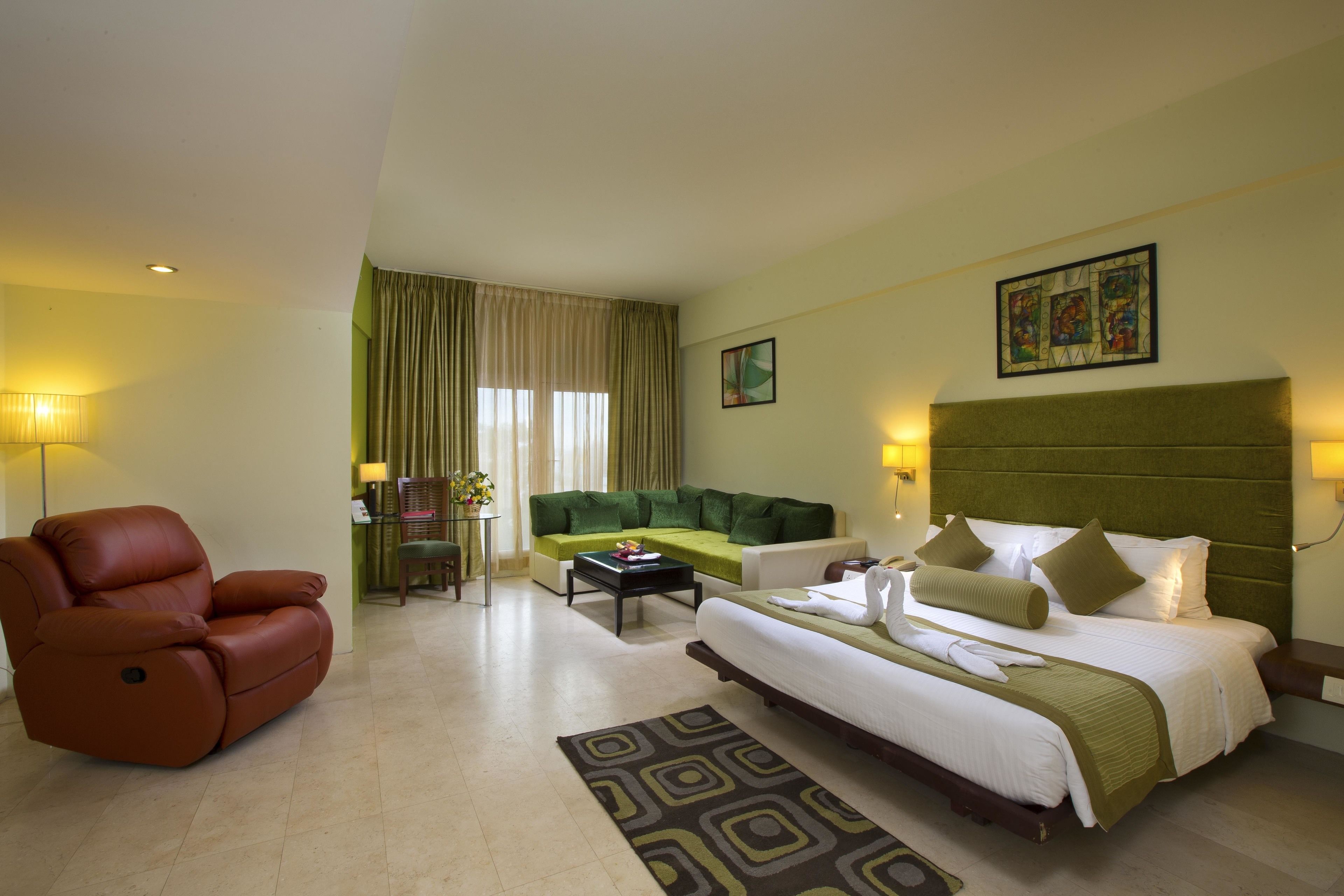 Una habitación de hotel con cama, sofá, sillón, mesa de centro y escritorio con lámpara.